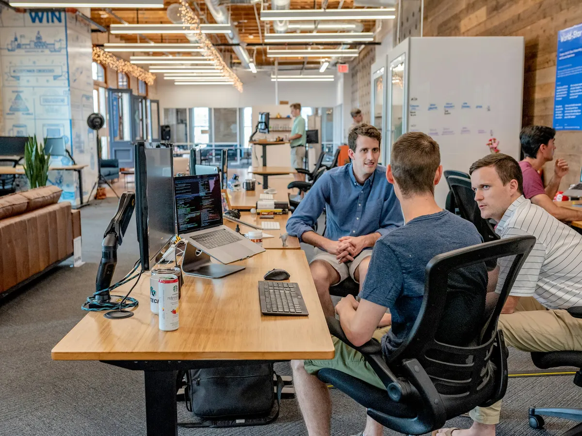 Colleagues discussing customer work around computer workstations in an office.