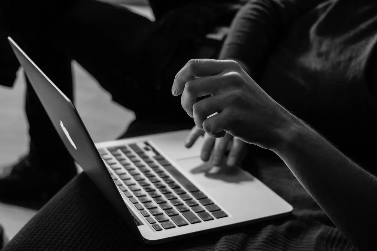 A close-up monochrome photograph of a person working on a laptop.